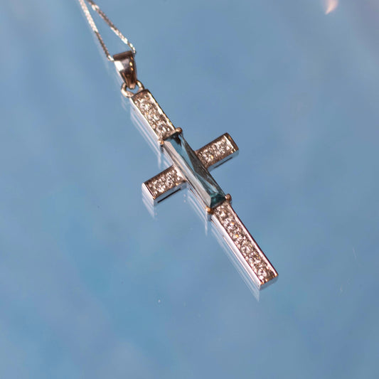 14-karat white gold cross pendant is a stunning piece of jewelry that features a scissor-cut aquamarine as its centerpiece, accented with sparkling diamonds.